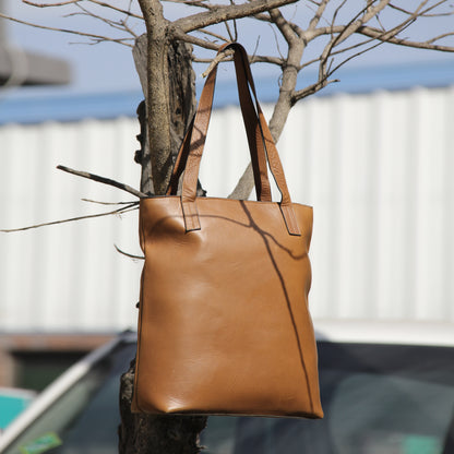 Structured cowhide leather bag in tan, featuring a minimalist exterior, multiple interior compartments, secure closures, adjustable straps, and durable craftsmanship for daily use