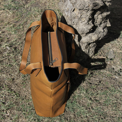 Structured cowhide leather bag in tan, featuring a minimalist exterior, multiple interior compartments, secure closures, adjustable straps, and durable craftsmanship for daily use
