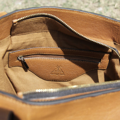 Structured cowhide leather bag in tan, featuring a minimalist exterior, multiple interior compartments, secure closures, adjustable straps, and durable craftsmanship for daily use