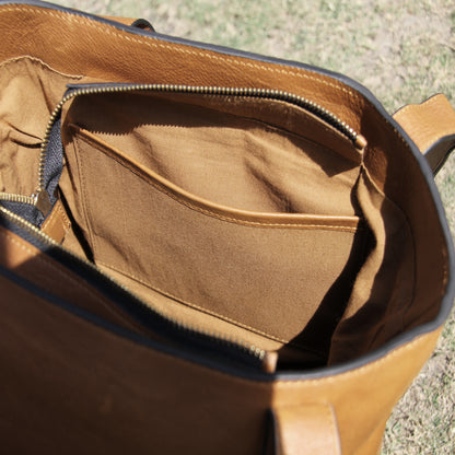 Structured cowhide leather bag in tan, featuring a minimalist exterior, multiple interior compartments, secure closures, adjustable straps, and durable craftsmanship for daily use
