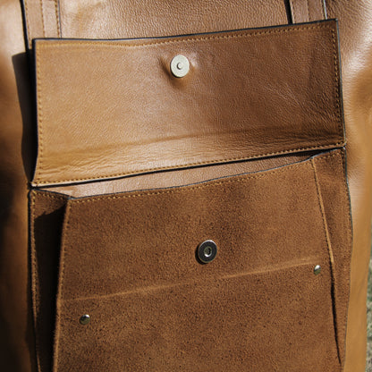 Structured cowhide leather bag in tan, featuring a minimalist exterior, multiple interior compartments, secure closures, adjustable straps, and durable craftsmanship for daily use