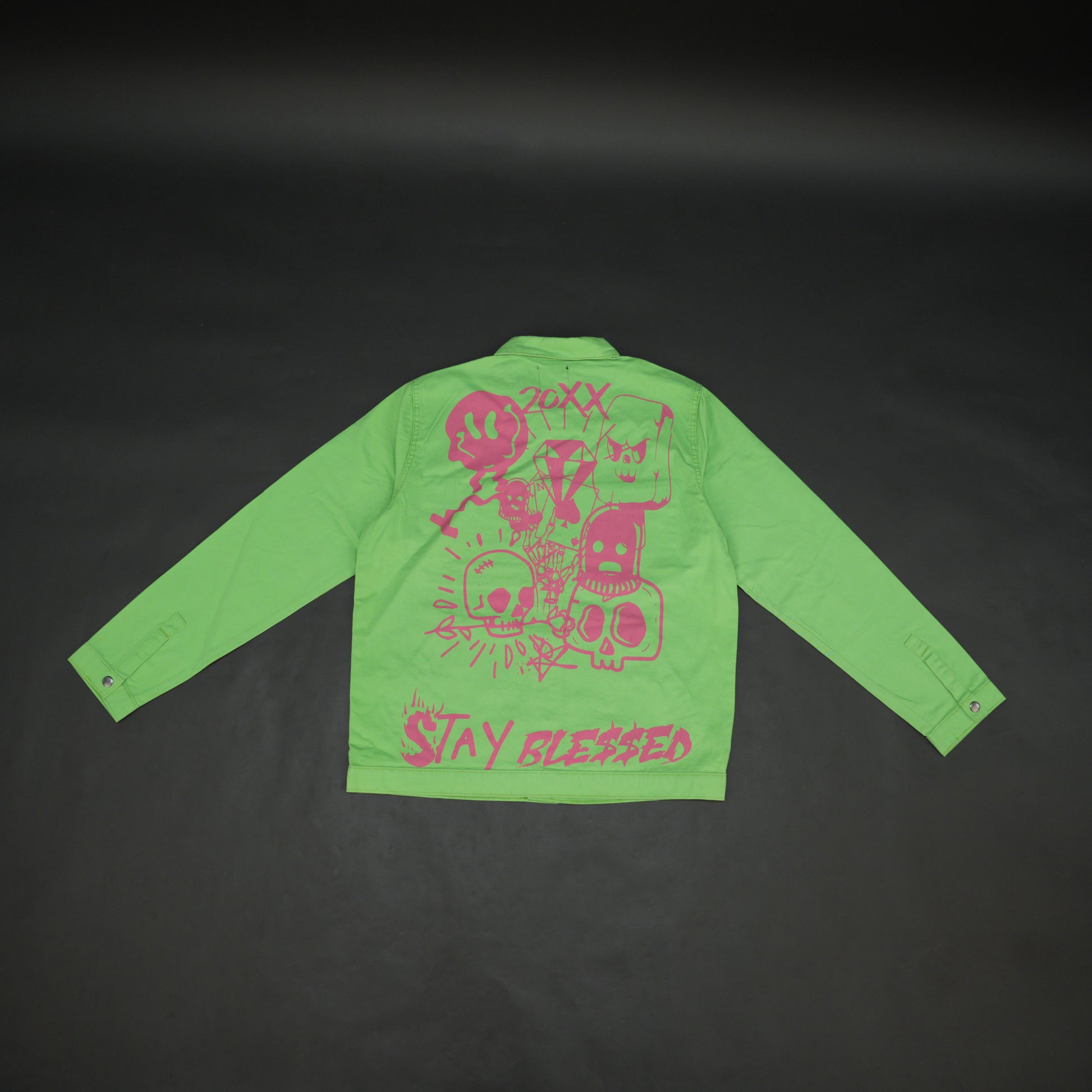 Green denim jacket with bold ‘Stay Blessed’ graphic on the back, button-down front, adjustable cuffs, and side pockets for casual wear