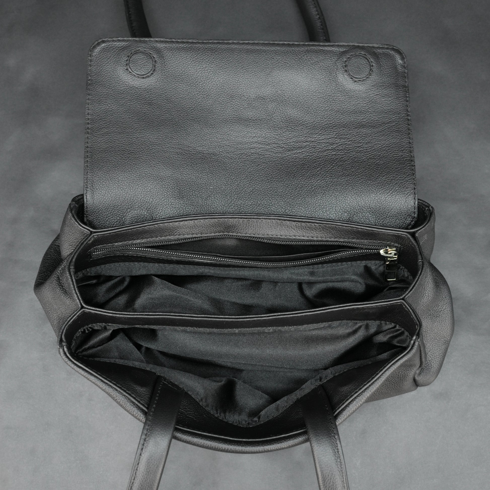 Black cow Chelsea leather bag with straps, compartments, and zipper pocket.